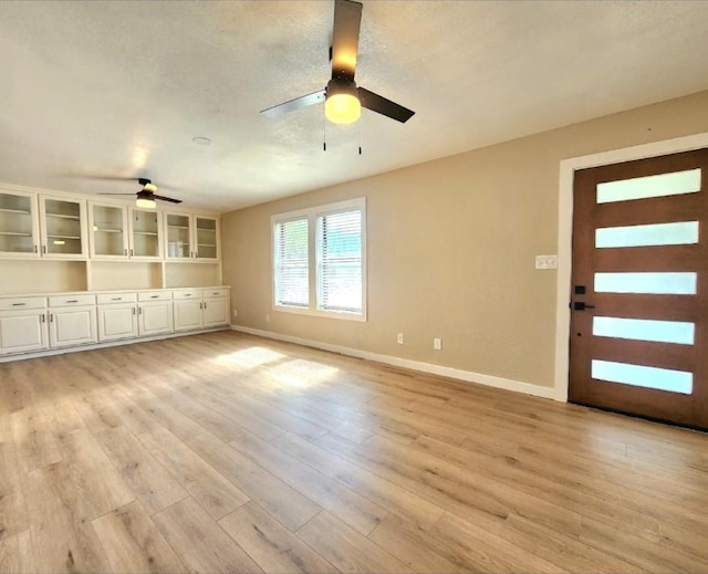 unfurnished living room with a ceiling fan, baseboards, and light wood-type flooring