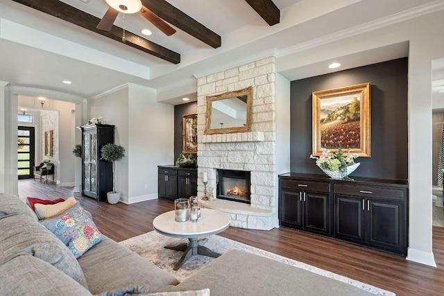 living room featuring crown molding, a ceiling fan, beamed ceiling, a fireplace, and dark wood-style flooring