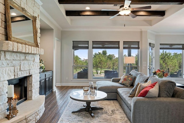living room with plenty of natural light, dark wood-type flooring, a ceiling fan, a fireplace, and beamed ceiling