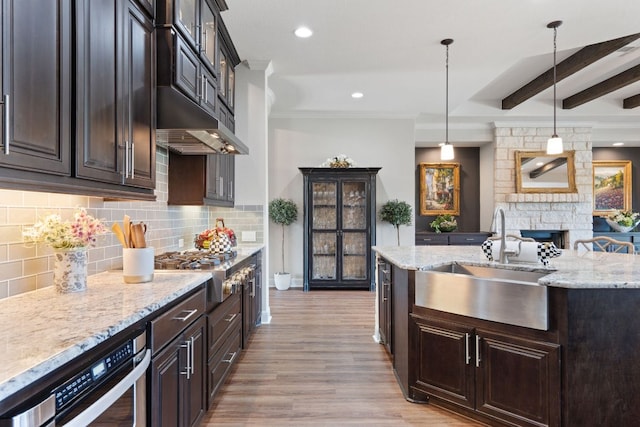 kitchen with a sink, light wood-style flooring, backsplash, light stone countertops, and hanging light fixtures