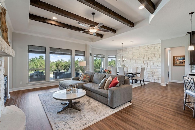 living room with ceiling fan, a stone fireplace, beam ceiling, dark wood-style flooring, and a chandelier