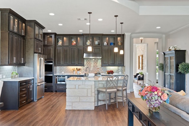 kitchen with stainless steel appliances, dark wood-style floors, decorative backsplash, dark brown cabinets, and crown molding