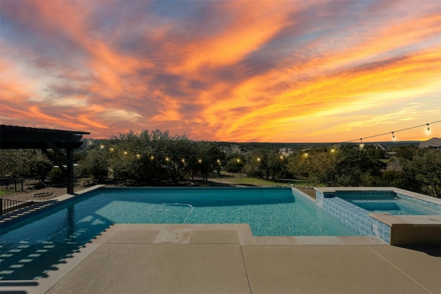 pool at dusk featuring a pool with connected hot tub