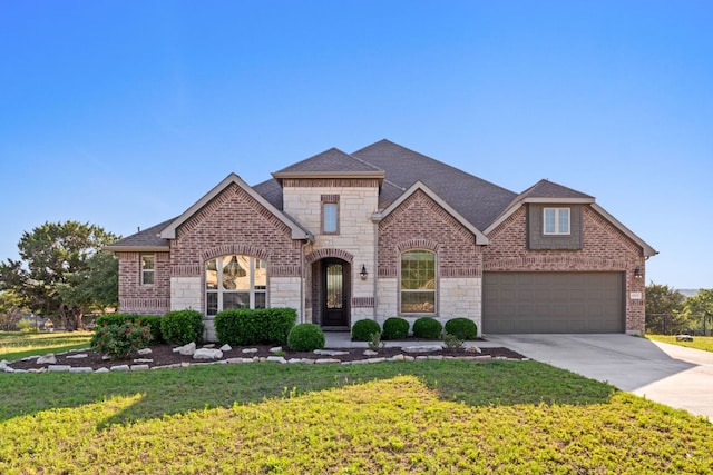 french provincial home featuring driveway, stone siding, a front yard, brick siding, and a shingled roof