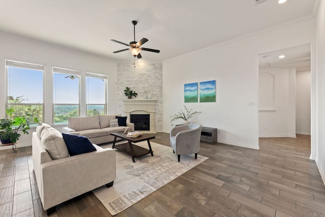 living room with a ceiling fan, ornamental molding, a stone fireplace, wood finished floors, and baseboards