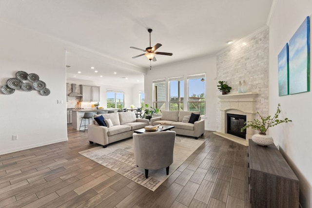 living area featuring ceiling fan, wood finished floors, a large fireplace, baseboards, and ornamental molding