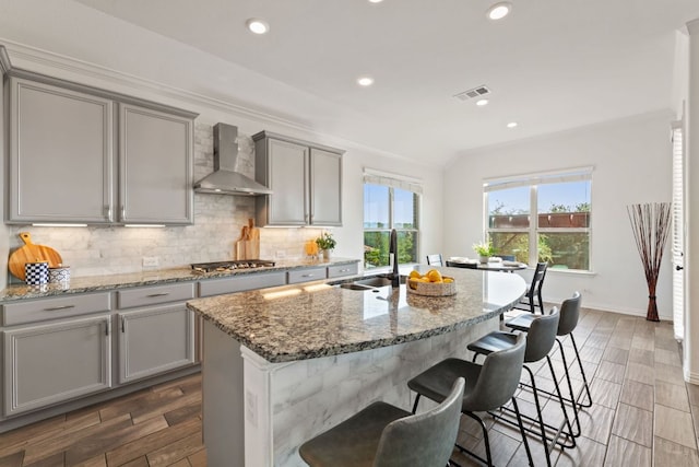 kitchen with wall chimney exhaust hood, gray cabinets, a sink, crown molding, and stainless steel gas cooktop