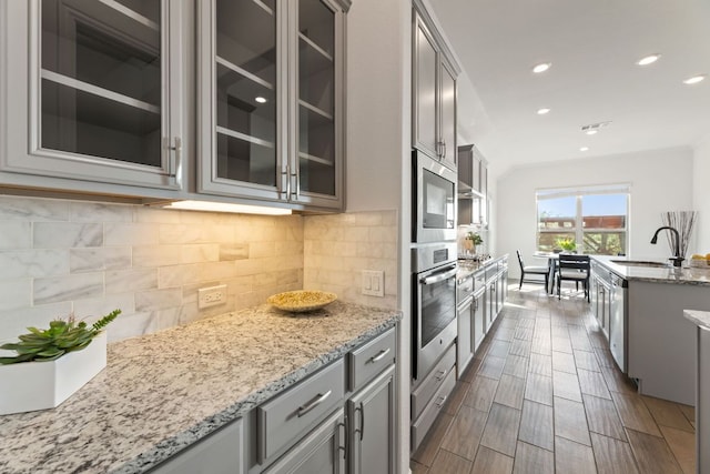 kitchen featuring stainless steel appliances, a sink, gray cabinets, glass insert cabinets, and recessed lighting