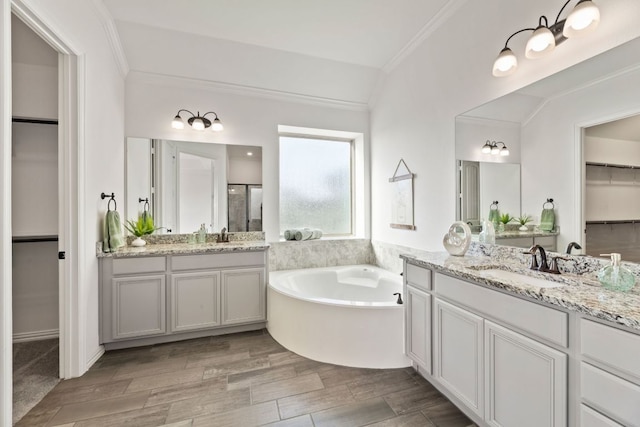 bathroom with ornamental molding, a bath, two vanities, a spacious closet, and wood finished floors