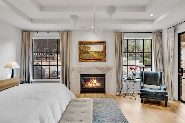 bedroom with a tray ceiling, wood finished floors, a premium fireplace, and access to exterior