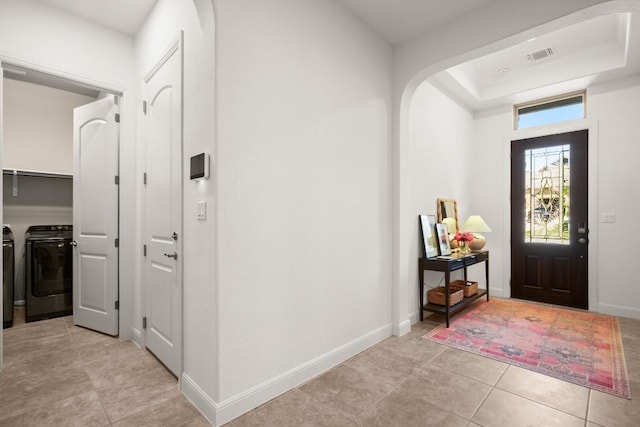 entrance foyer featuring washing machine and dryer, light tile patterned flooring, arched walkways, baseboards, and a raised ceiling