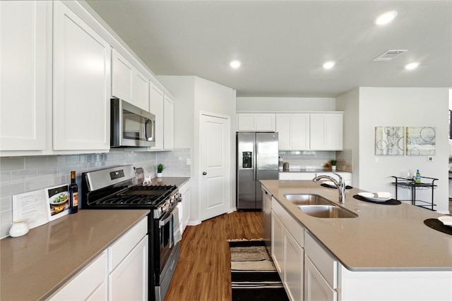 10207 Buster Dr, Austin, TX 78748 - kitchen featuring appliances with stainless steel finishes, a sink, dark wood-style floors, decorative backsplash, and a center island with sink