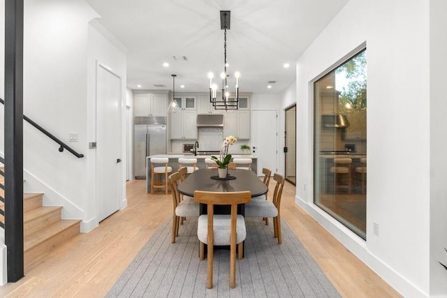 dining area featuring light wood-style floors, recessed lighting, baseboards, a chandelier, and stairs