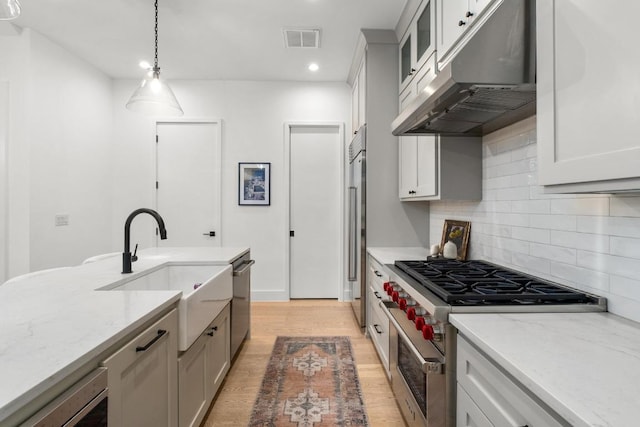 kitchen with under cabinet range hood, premium appliances, a sink, decorative backsplash, and recessed lighting