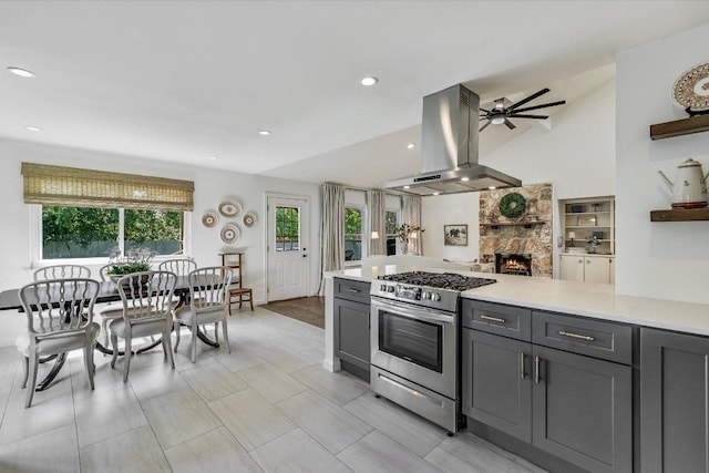 kitchen with island range hood, stainless steel gas stove, open shelves, gray cabinetry, and light countertops