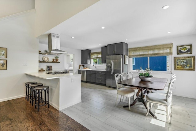 kitchen with appliances with stainless steel finishes, island range hood, light countertops, a kitchen bar, and a peninsula