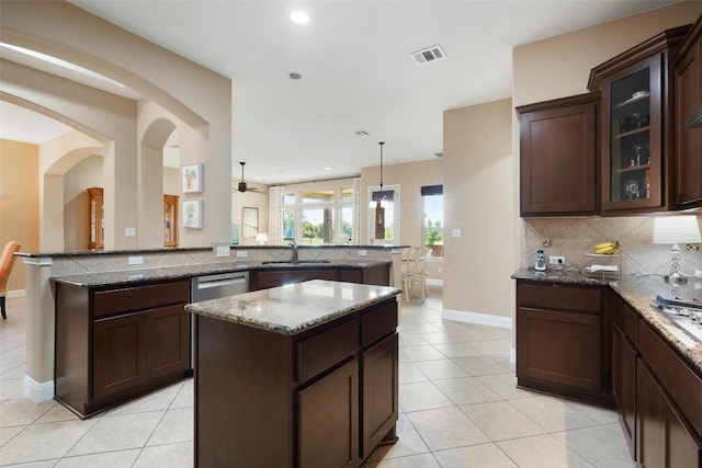 kitchen featuring light tile patterned flooring, tasteful backsplash, dark stone countertops, glass insert cabinets, and dark brown cabinetry