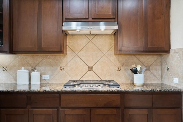 kitchen with ventilation hood, stainless steel gas cooktop, decorative backsplash, stone counters, and dark brown cabinetry