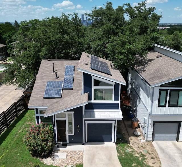 view of front of house featuring a garage, roof mounted solar panels, fence, a shingled roof, and concrete driveway