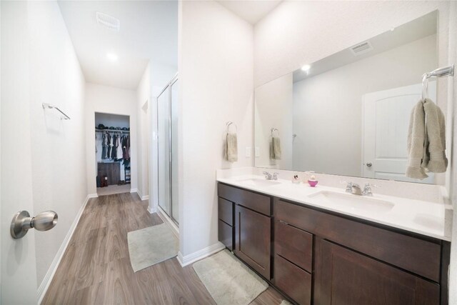 full bath with wood finished floors, a stall shower, a spacious closet, double vanity, and baseboards