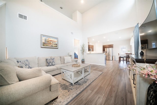 living room featuring light wood-type flooring, a towering ceiling, and baseboards