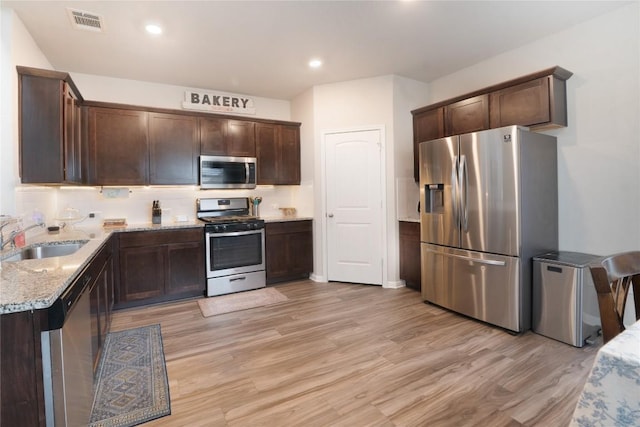 kitchen featuring stainless steel appliances, a sink, dark brown cabinetry, light stone counters, and light wood-style flooring