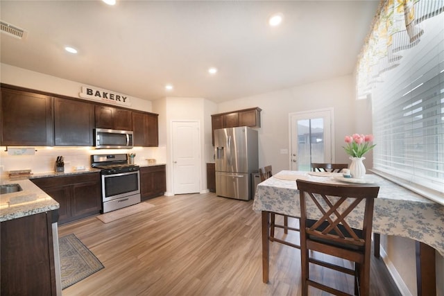 kitchen with appliances with stainless steel finishes, dark brown cabinetry, light wood-style floors, recessed lighting, and light stone countertops