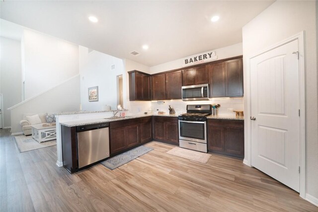 kitchen featuring appliances with stainless steel finishes, light wood-style floors, dark brown cabinetry, tasteful backsplash, and a sink