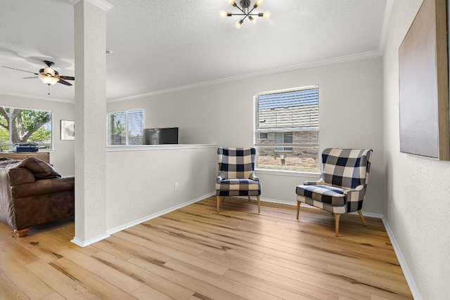 living area featuring ornamental molding, light wood-style floors, baseboards, a textured ceiling, and a ceiling fan