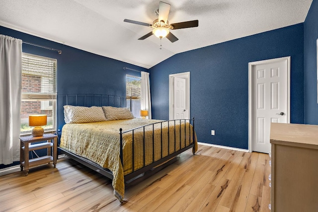 bedroom featuring vaulted ceiling, light wood finished floors, ceiling fan, a textured wall, and baseboards