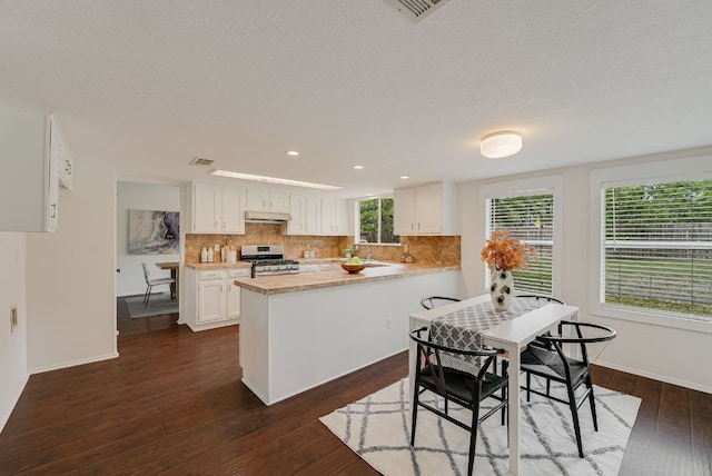 kitchen featuring stainless steel gas range, under cabinet range hood, a peninsula, white cabinets, and light countertops