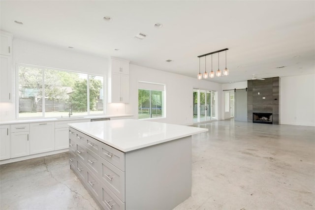 kitchen featuring finished concrete floors, light countertops, a center island, white cabinetry, and a large fireplace