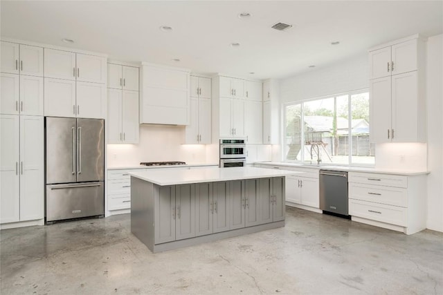 kitchen featuring stainless steel appliances, concrete floors, white cabinetry, light countertops, and a kitchen island