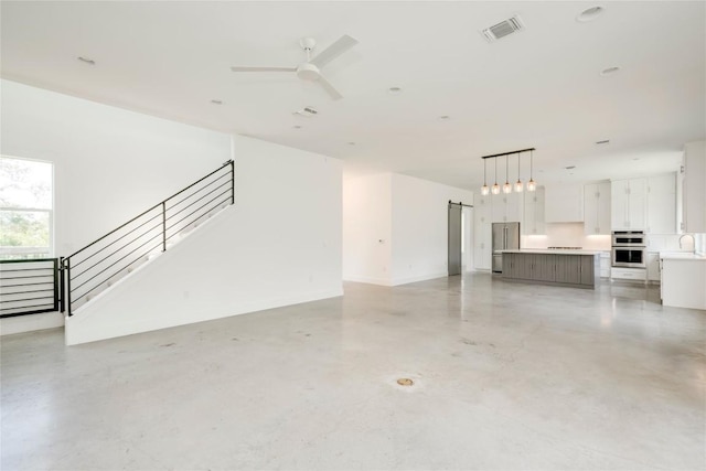 unfurnished living room featuring concrete flooring, stairway, a sink, and a ceiling fan