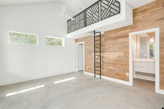empty room featuring wooden walls, concrete flooring, a high ceiling, ceiling fan, and baseboards