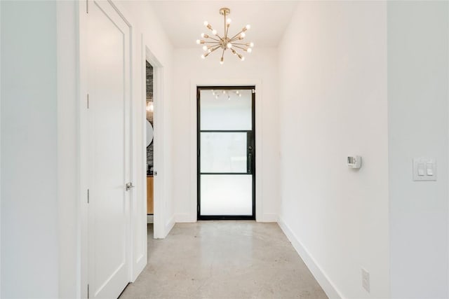 hall featuring a chandelier, concrete floors, and baseboards