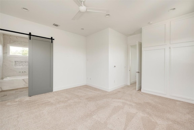 1305 Village W Dr, Austin, TX 78733 - unfurnished bedroom featuring light colored carpet, connected bathroom, a barn door, and ceiling fan