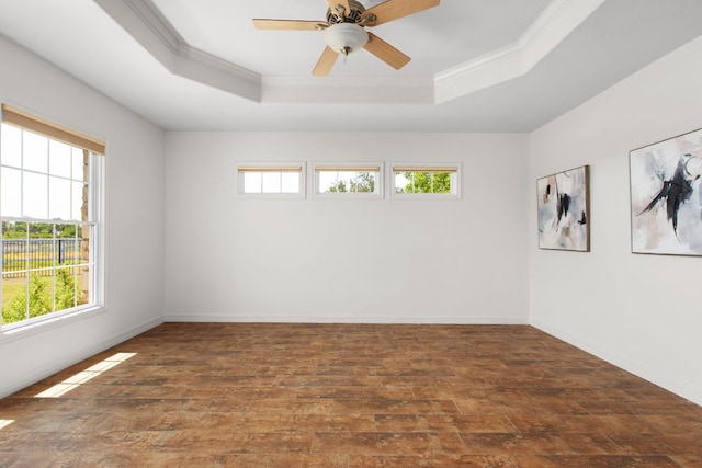 empty room featuring a raised ceiling, hardwood / wood-style flooring, ornamental molding, baseboards, and ceiling fan