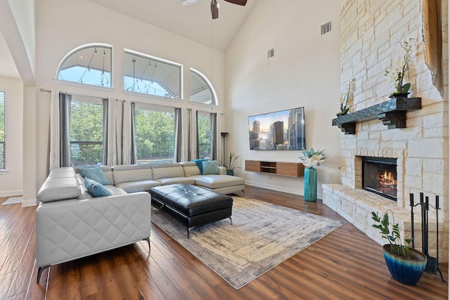 living area featuring ceiling fan, high vaulted ceiling, baseboards, wood finished floors, and a stone fireplace
