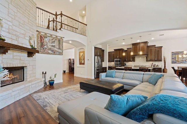 living area with arched walkways, wood finished floors, a stone fireplace, a towering ceiling, and baseboards
