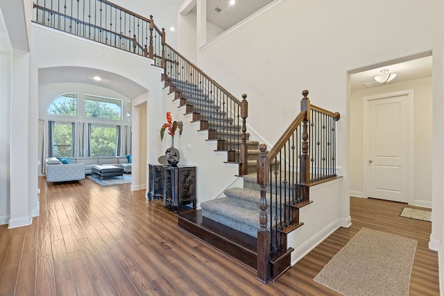 stairs featuring a towering ceiling, wood finished floors, arched walkways, and baseboards