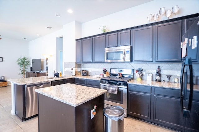 411 Tilly Ln, Buda, TX 78610 - kitchen with stainless steel appliances, light tile patterned floors, light stone counters, a center island, and a peninsula