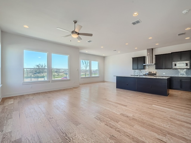 kitchen featuring stainless steel appliances, open floor plan, wall chimney range hood, a ceiling fan, and recessed lighting