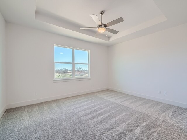 unfurnished room with a raised ceiling, light carpet, baseboards, and ceiling fan