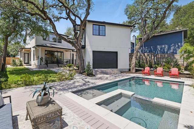 rear view of house featuring a pool with connected hot tub, fence, stucco siding, and a garage