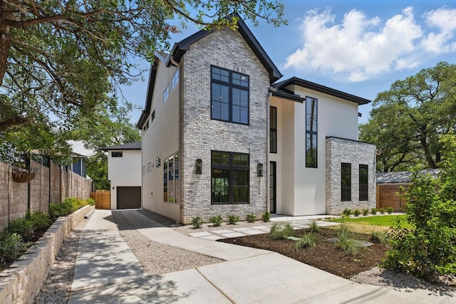 contemporary house with stucco siding, fence, driveway, and brick siding