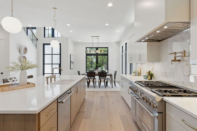 kitchen with stainless steel appliances, wall chimney range hood, light wood finished floors, light countertops, and a sink