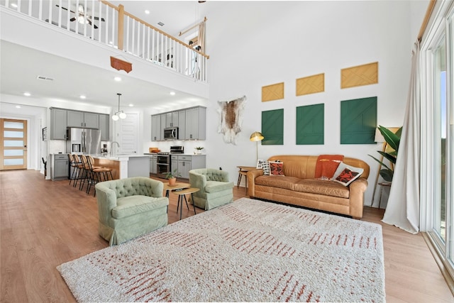 living area featuring healthy amount of natural light, light wood-style floors, a high ceiling, and recessed lighting