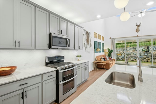 kitchen featuring appliances with stainless steel finishes, a sink, gray cabinets, tasteful backsplash, and light stone counters
