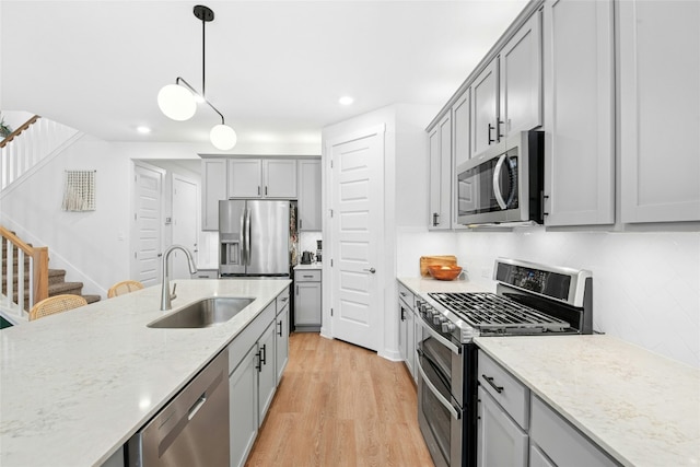 kitchen featuring appliances with stainless steel finishes, a sink, gray cabinets, recessed lighting, and light wood finished floors